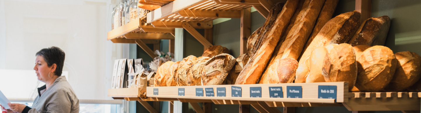 Dona en una fleca amb prestatgeries plenes de pans artesans